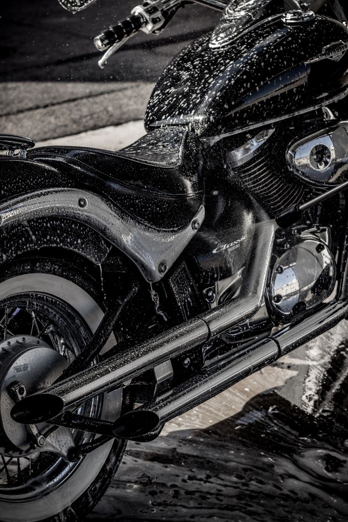 Close-up of a sleek motorcycle being washed, highlighting shiny chrome details and wet texture.