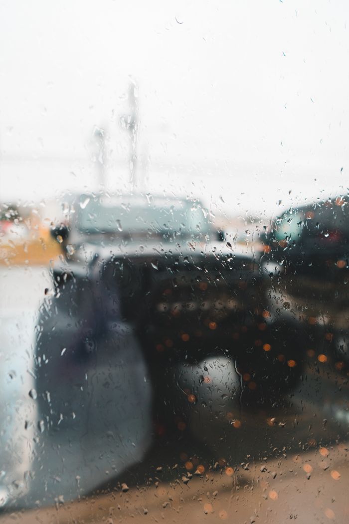 Transparent glass wall with pure aqua drips against parked transport in city on rainy day